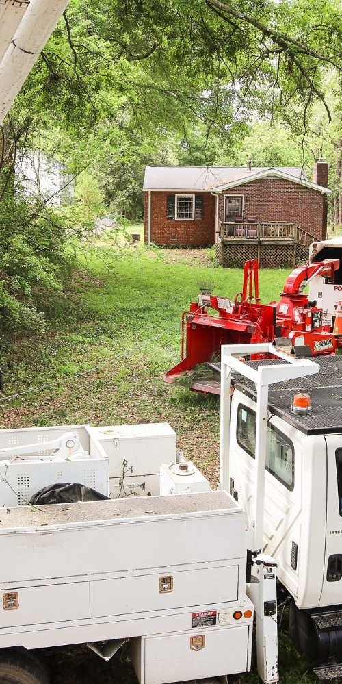 A high-angle view of a red wood chipper and white service truck parked in a grassy backyard behind a brick home in Loganville.