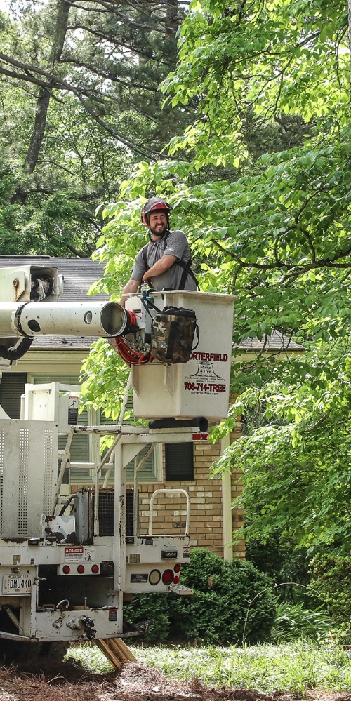 A smiling Porterfield team member in a safety helmet working from a bucket lift on a residential property in Buckhead, Georgia.