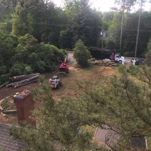 A wide view of a residential lot in Bostwick being cleared of logs and debris using a Bobcat loader and a wood chipper.