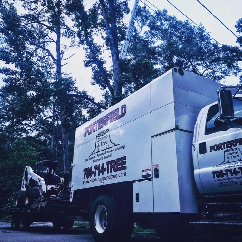 A white Porterfield service truck hauling a Bobcat loader on a trailer for a large-scale tree service project in Buckhead, Georgia.
